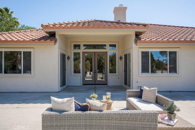 rear view of property featuring a tiled roof, french doors, a patio, and stucco siding