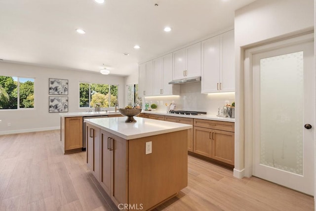 kitchen with backsplash, a kitchen island, under cabinet range hood, light countertops, and gas cooktop