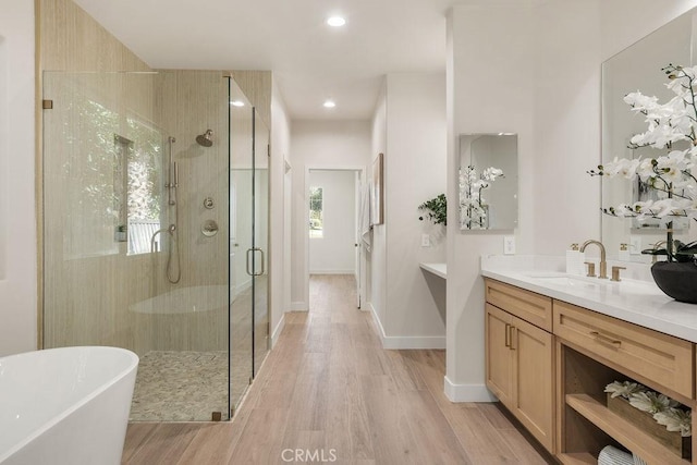 bathroom featuring a shower stall, baseboards, wood finished floors, a freestanding tub, and vanity