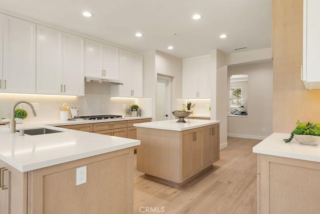 kitchen featuring gas cooktop, light countertops, under cabinet range hood, and a sink