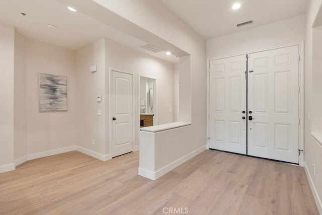 foyer entrance with light wood-type flooring, baseboards, and visible vents