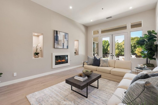 living room with light wood finished floors, visible vents, baseboards, french doors, and a glass covered fireplace