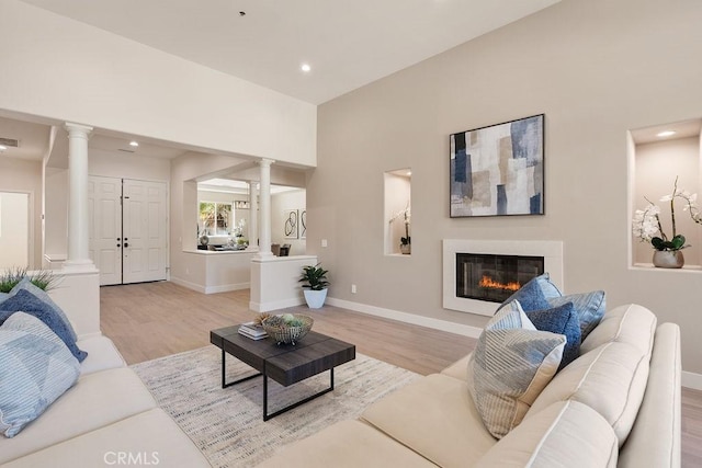 living area with light wood finished floors, visible vents, baseboards, decorative columns, and a glass covered fireplace