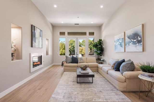 living area featuring a glass covered fireplace, french doors, baseboards, and light wood finished floors