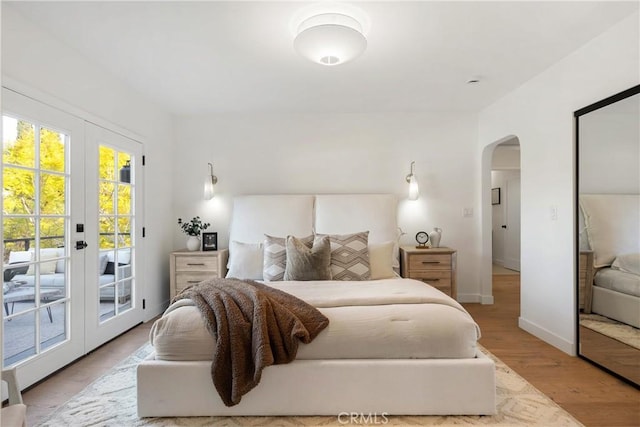 bedroom with baseboards, arched walkways, wood finished floors, access to outside, and french doors