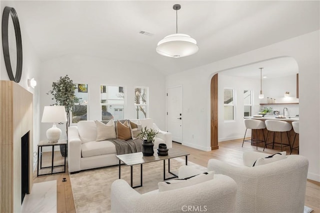 living room with arched walkways, light wood finished floors, visible vents, vaulted ceiling, and baseboards