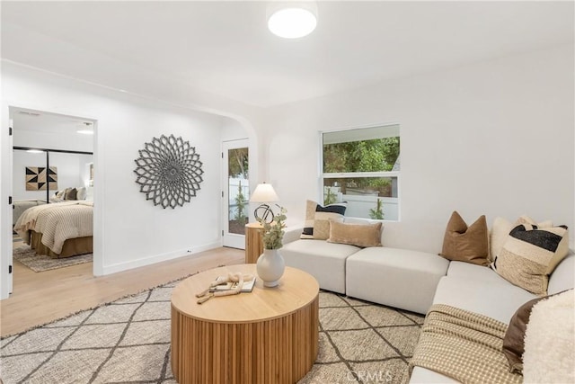 living area with arched walkways, light wood finished floors, and baseboards