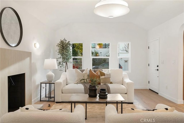 living room with a fireplace, arched walkways, vaulted ceiling, and wood finished floors