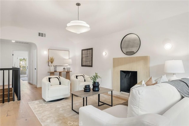 living area with arched walkways, visible vents, lofted ceiling, and light wood finished floors