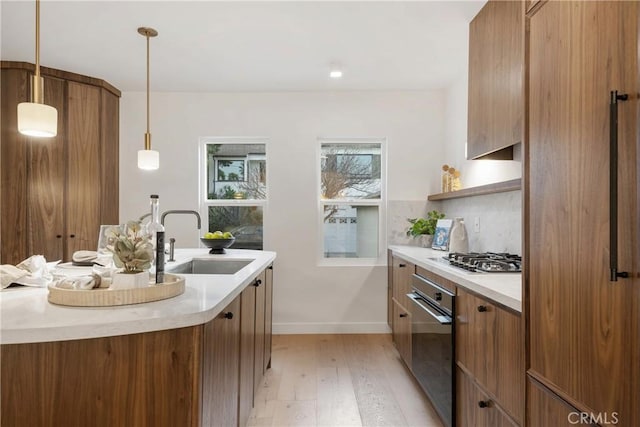 kitchen featuring light countertops, stainless steel gas stovetop, brown cabinetry, a sink, and oven