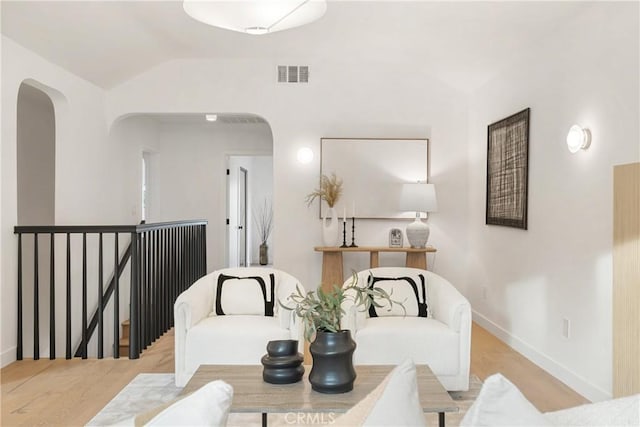 sitting room with lofted ceiling, arched walkways, an upstairs landing, and visible vents