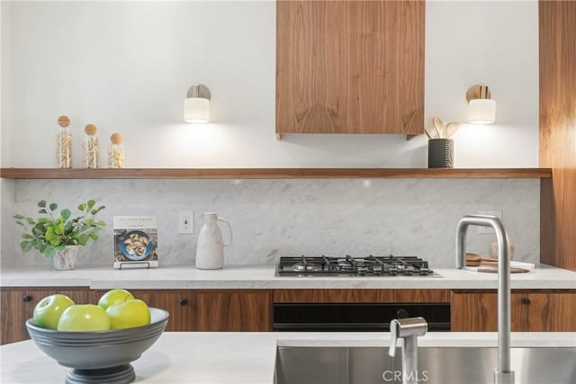 kitchen with modern cabinets, brown cabinets, light countertops, stainless steel gas cooktop, and backsplash