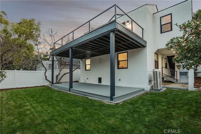 back of property at dusk with stucco siding, fence, a lawn, and a patio