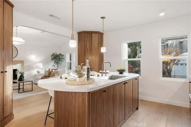 kitchen with light wood-style flooring, brown cabinetry, a sink, and light countertops