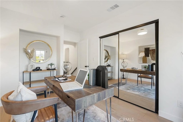 home office with light wood-style flooring, visible vents, and baseboards