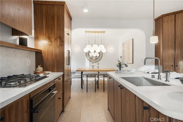 kitchen with oven, a sink, light countertops, light wood-type flooring, and stainless steel gas stovetop