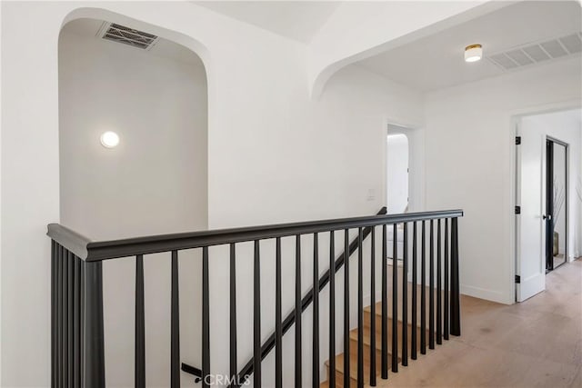 hall with an upstairs landing, baseboards, visible vents, and light wood finished floors