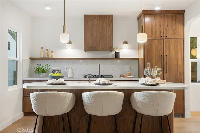 kitchen with light countertops, tasteful backsplash, light wood-style floors, and brown cabinets