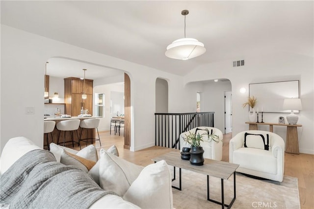 living room featuring arched walkways, visible vents, vaulted ceiling, light wood-type flooring, and baseboards