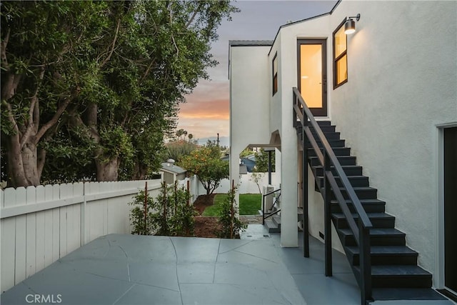 patio terrace at dusk featuring stairs and fence