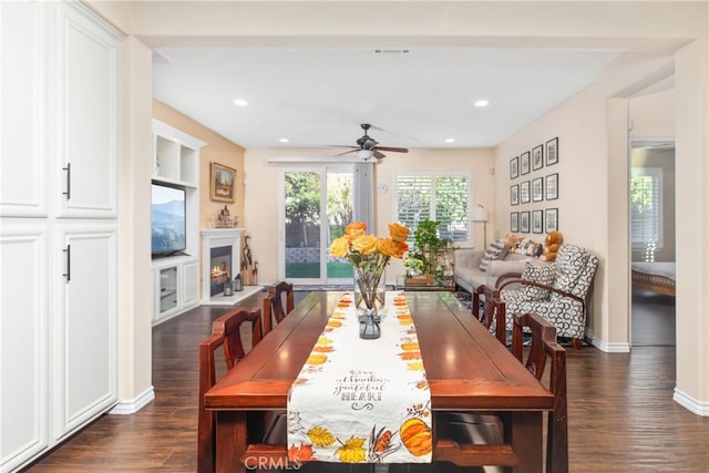 dining space with a warm lit fireplace, dark wood-style flooring, baseboards, and recessed lighting