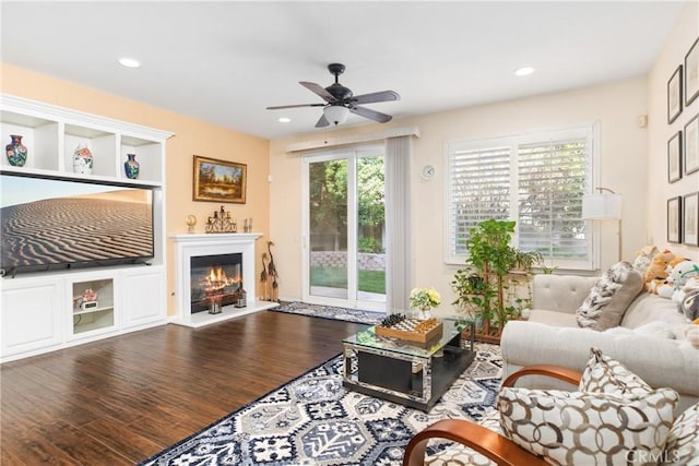 living area with ceiling fan, a glass covered fireplace, wood finished floors, and recessed lighting