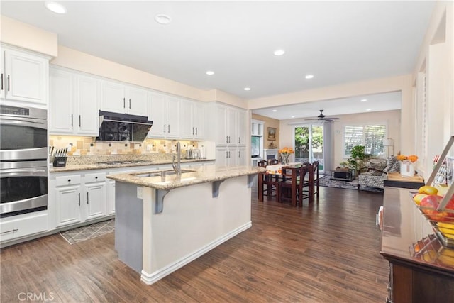 kitchen with dark wood finished floors, a breakfast bar, stainless steel appliances, white cabinetry, and a sink