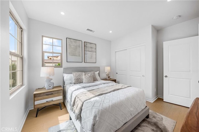 bedroom with light wood-style floors, baseboards, visible vents, and a closet