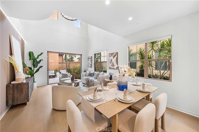 dining room with light wood-style floors, recessed lighting, a towering ceiling, and baseboards