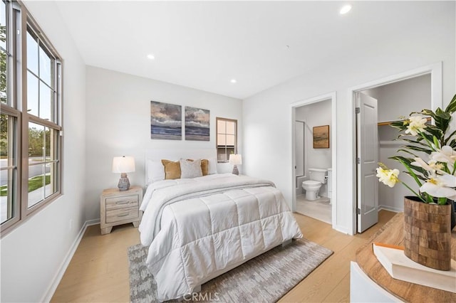 bedroom with baseboards, light wood-style flooring, ensuite bathroom, a spacious closet, and recessed lighting