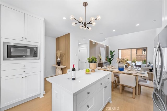 kitchen with white cabinets, light countertops, freestanding refrigerator, built in microwave, and light wood finished floors