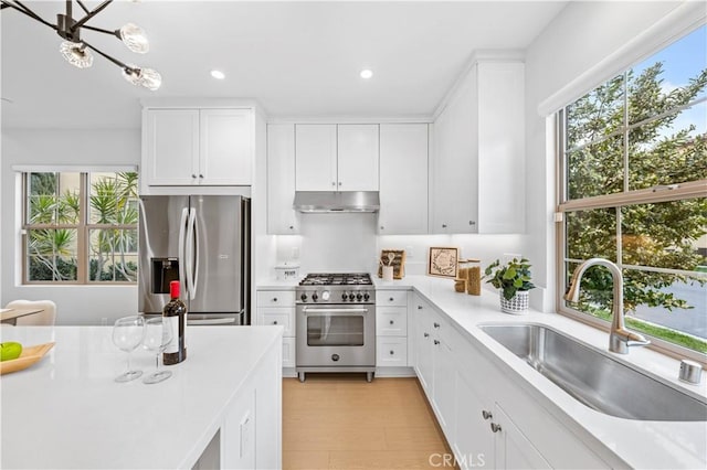 kitchen featuring stainless steel appliances, light countertops, a sink, plenty of natural light, and under cabinet range hood