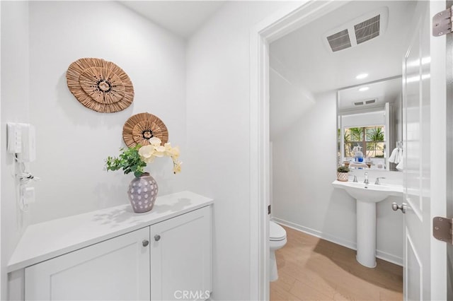 half bathroom with baseboards, visible vents, toilet, and wood finished floors