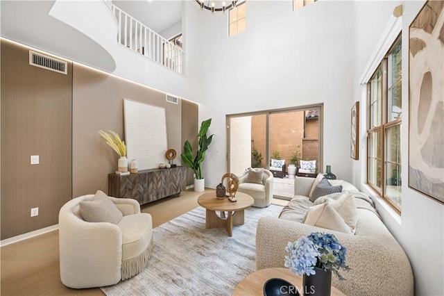 living area featuring a towering ceiling, wood finished floors, visible vents, and an inviting chandelier