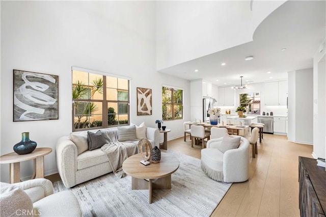 living area with a healthy amount of sunlight, light wood finished floors, a towering ceiling, and recessed lighting