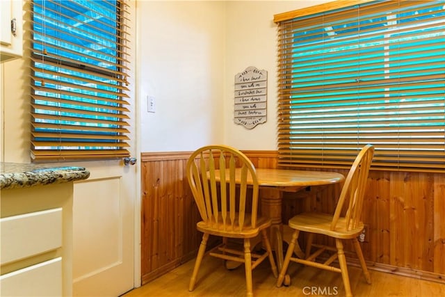 dining area with a wainscoted wall, wooden walls, and wood finished floors