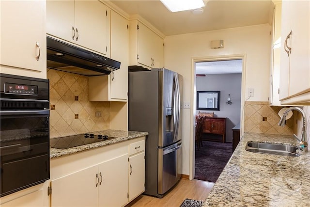 kitchen with decorative backsplash, under cabinet range hood, light wood-type flooring, black appliances, and a sink