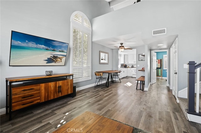 living room featuring a high ceiling, visible vents, baseboards, and wood finished floors