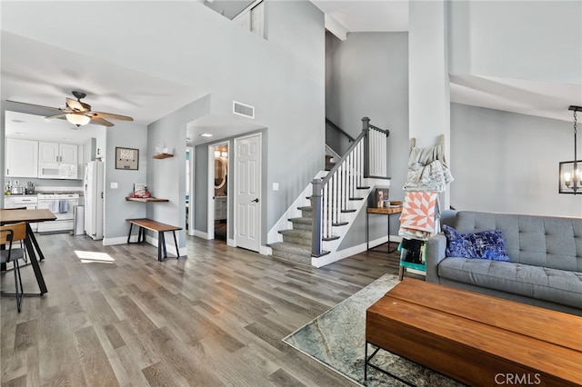 living area featuring visible vents, stairway, wood finished floors, baseboards, and ceiling fan with notable chandelier