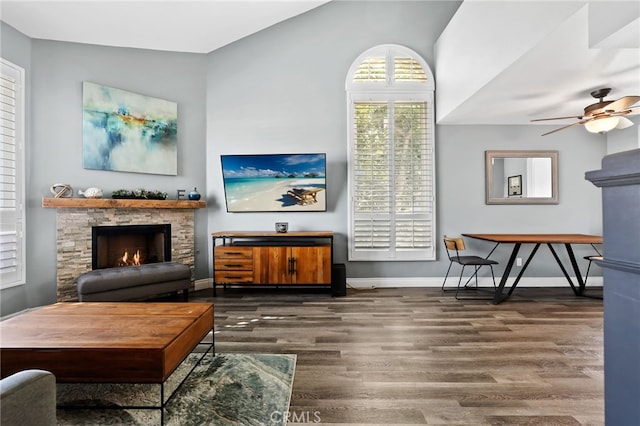 living room featuring ceiling fan, a fireplace, baseboards, and wood finished floors