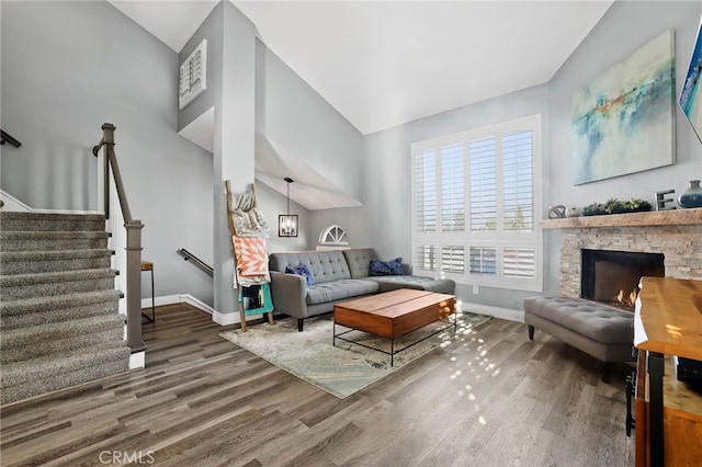 living room featuring baseboards, lofted ceiling, wood finished floors, stairs, and a stone fireplace