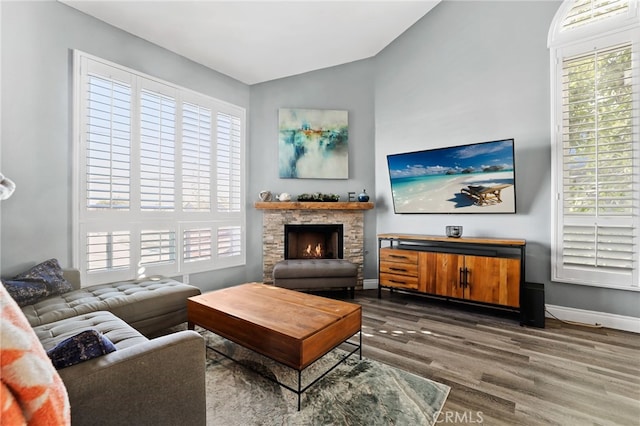 living area featuring vaulted ceiling, a stone fireplace, baseboards, and wood finished floors