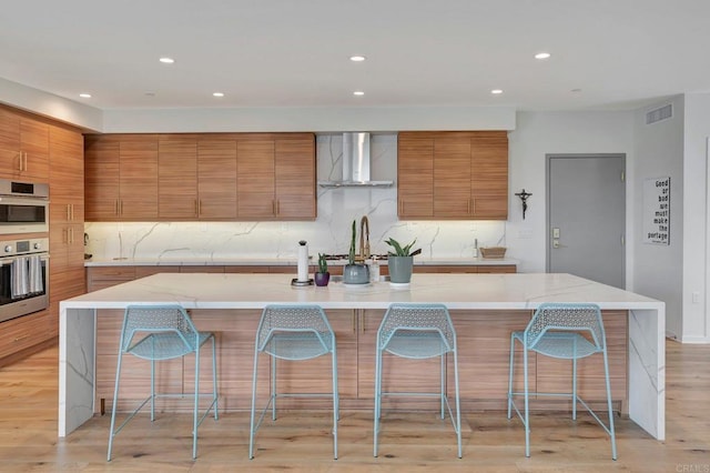 kitchen featuring brown cabinetry, a breakfast bar, visible vents, and wall chimney range hood