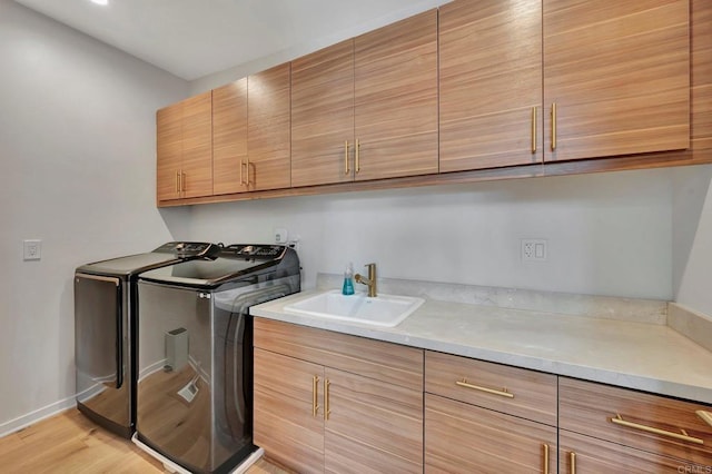 laundry room featuring cabinet space, a sink, separate washer and dryer, light wood-type flooring, and baseboards