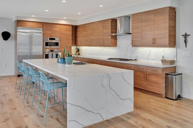 kitchen with tasteful backsplash, brown cabinetry, stainless steel appliances, wall chimney range hood, and a kitchen bar