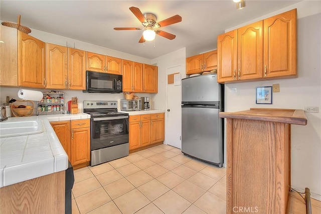 kitchen with a ceiling fan, tile countertops, a sink, light tile patterned floors, and stainless steel appliances
