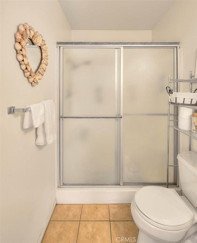 bathroom with toilet, a shower with door, baseboards, and tile patterned flooring