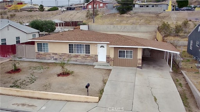 ranch-style house with stucco siding, driveway, stone siding, fence, and roof with shingles