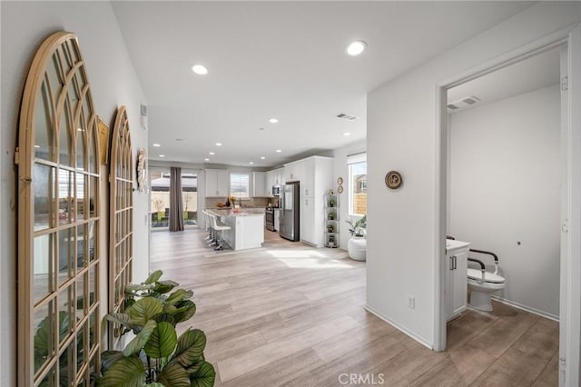 corridor featuring light wood finished floors, visible vents, and recessed lighting