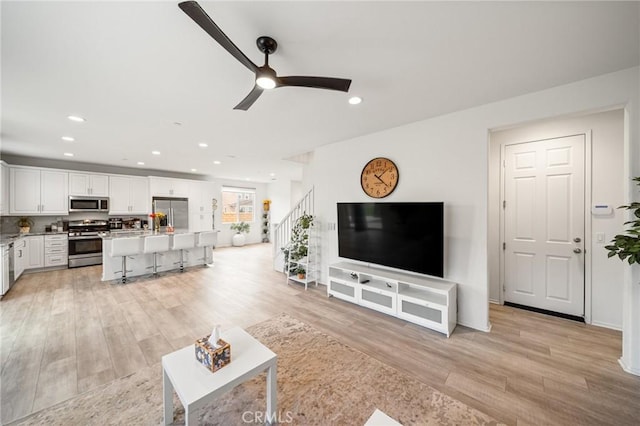 living area featuring light wood-type flooring, ceiling fan, recessed lighting, and stairs